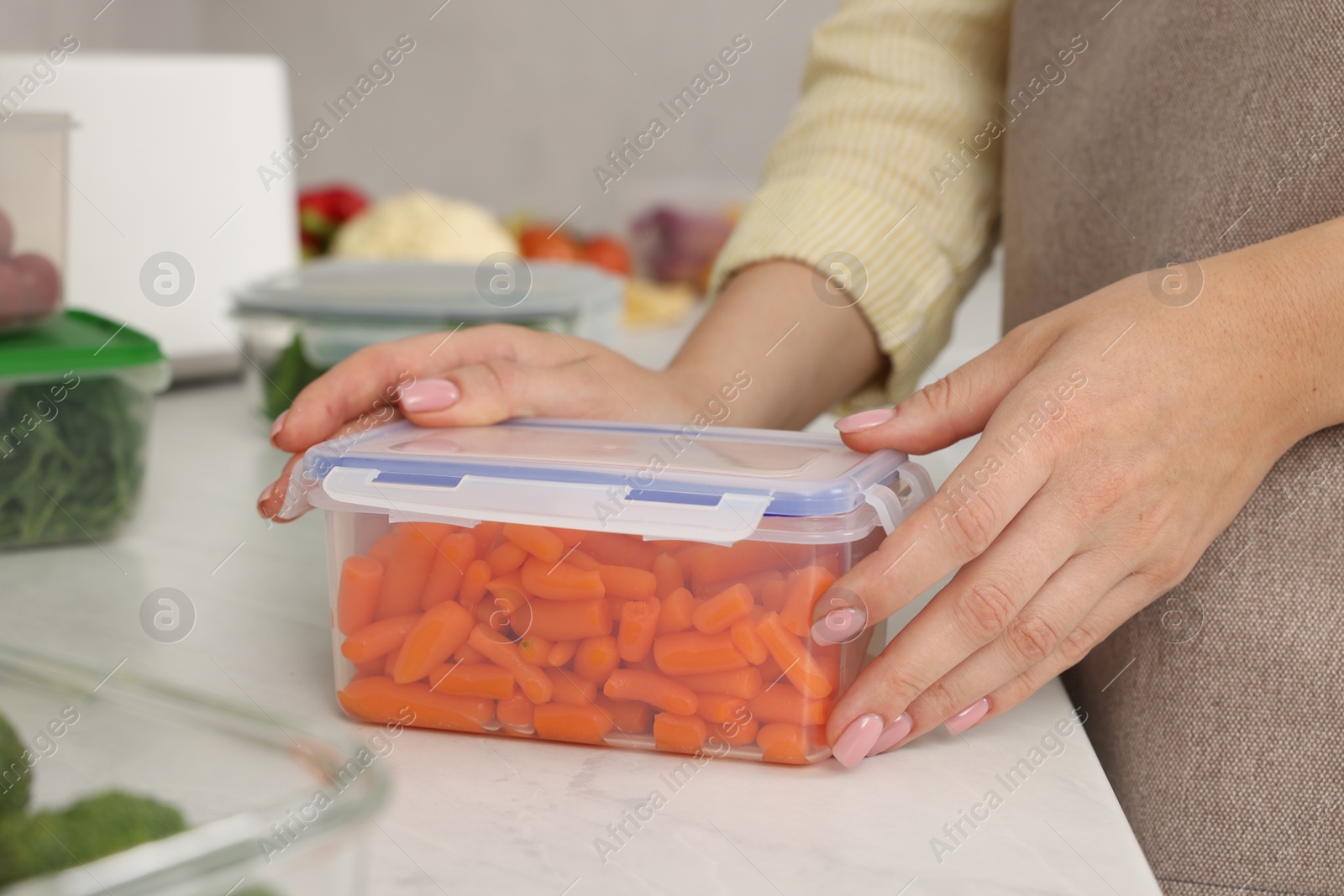 Photo of Woman sealing container with lid at white marble table in kitchen, closeup. Food storage