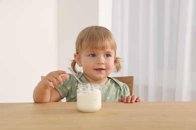 Photo of Cute little child eating tasty yogurt with spoon at wooden table indoors