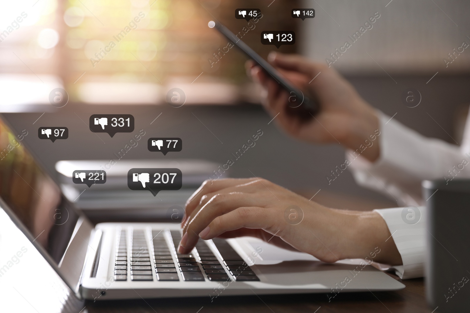 Image of Closeup view of young woman using modern laptop with smartphone indoors and virtual dislike icons at table. Cyberbullying concept