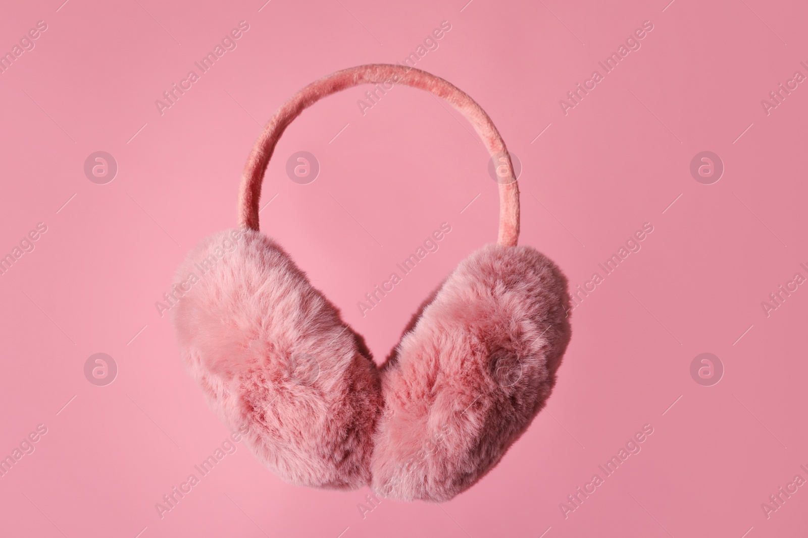 Photo of Fluffy earmuffs on pink background. Stylish winter accessory