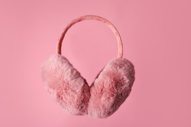 Photo of Fluffy earmuffs on pink background. Stylish winter accessory