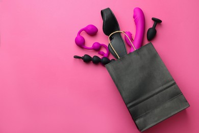 Photo of Shopping bag with different sex toys on pink background, flat lay. Space for text