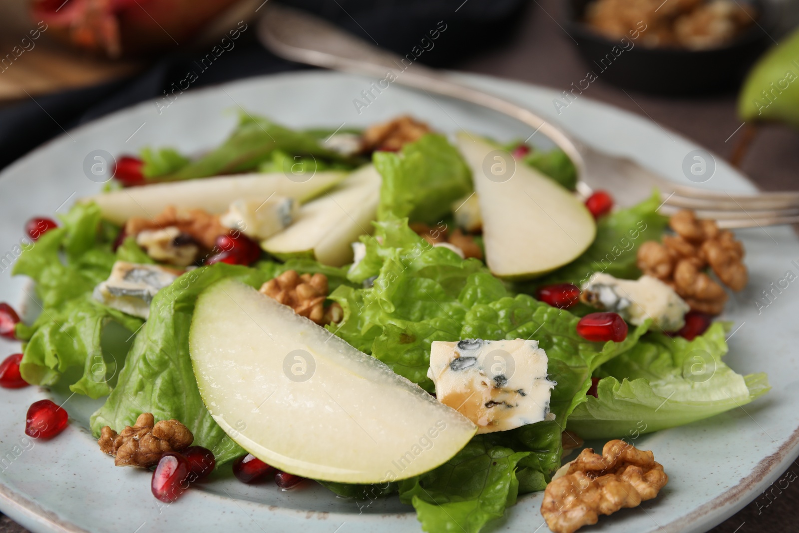 Photo of Delicious pear salad with lettuce, blue cheese, pomegranate and walnuts on plate, closeup