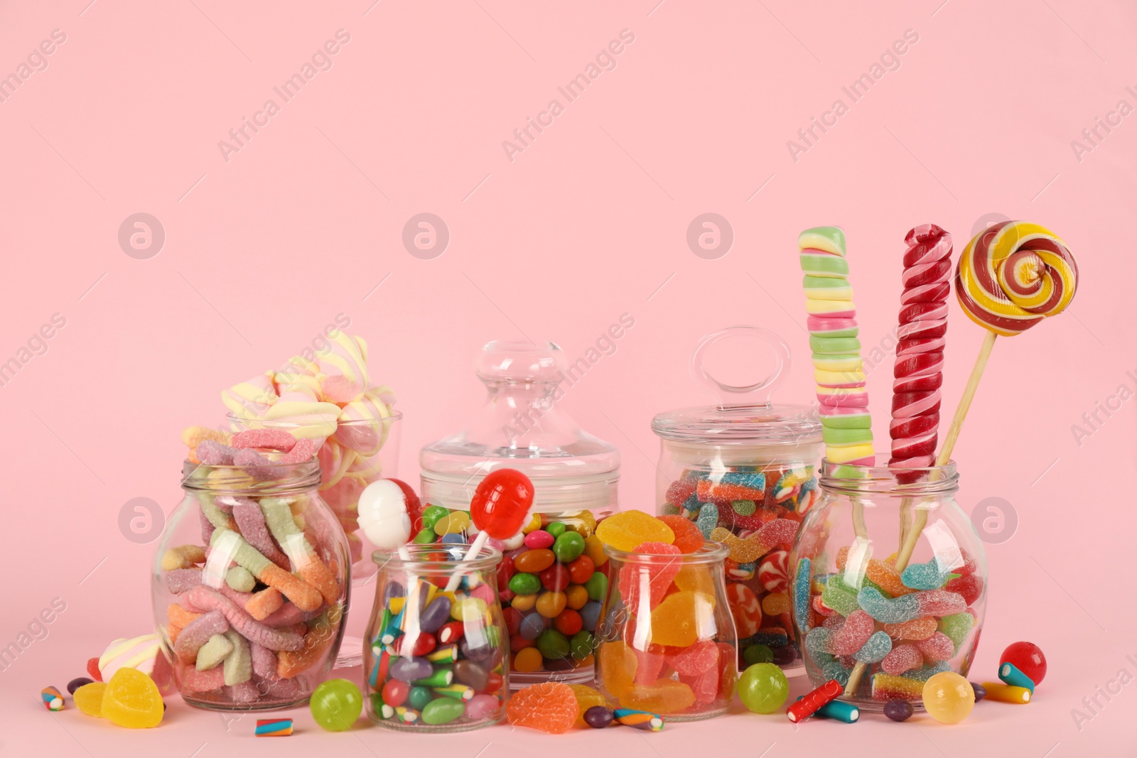 Photo of Glass jars with lots of different candies on pink background