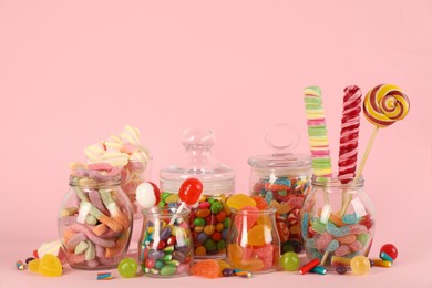 Glass jars with lots of different candies on pink background