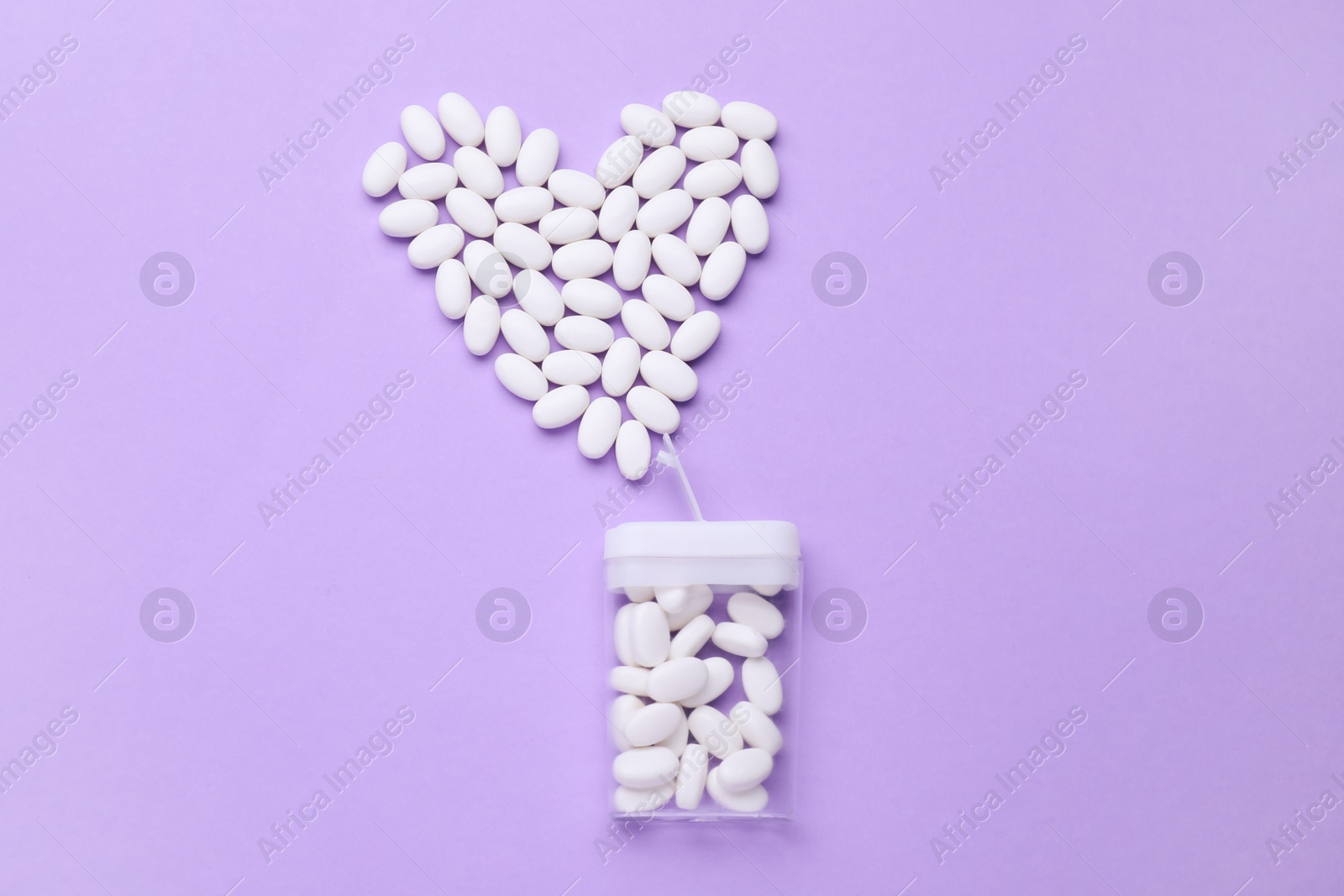 Photo of Heart made of tasty dragee candies and container on lilac background, flat lay