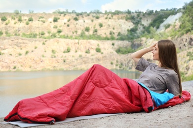 Young camper in sleeping bag on cliff near lake