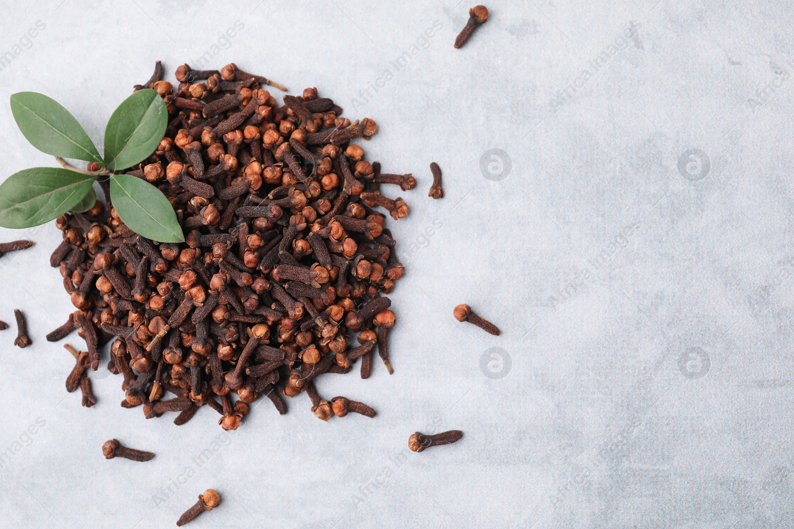 Photo of Pile of aromatic dried clove buds and leaves on grey table, top view. Space for text