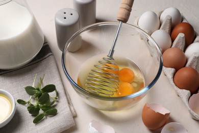 Metal whisk, raw eggs in bowl and ingredients on light table