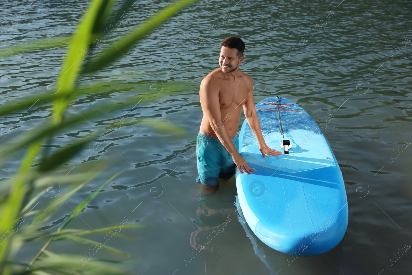 Photo of Man standing near SUP board in river water on sunny day