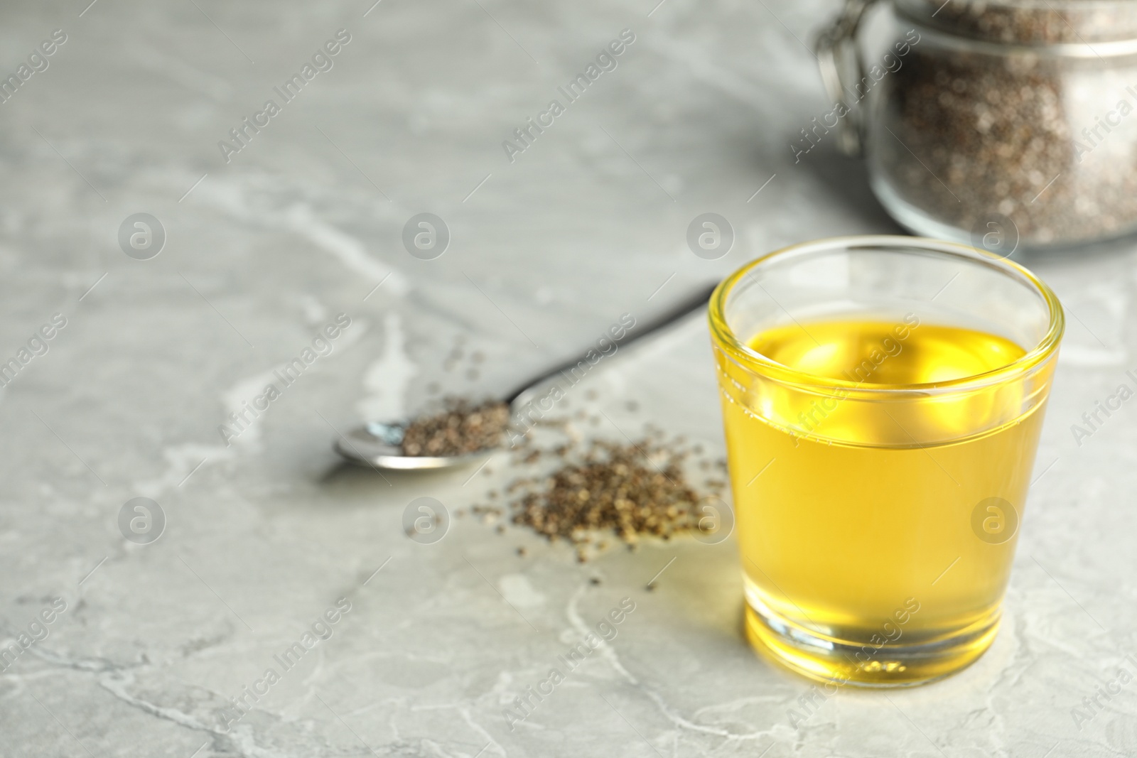 Photo of Glass of chia seeds oil on grey table, closeup. Space for text