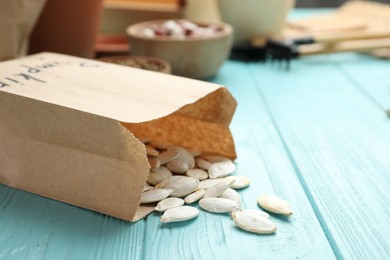 Photo of Paper bag with raw pumpkin seeds on blue wooden table, closeup. Vegetable planting