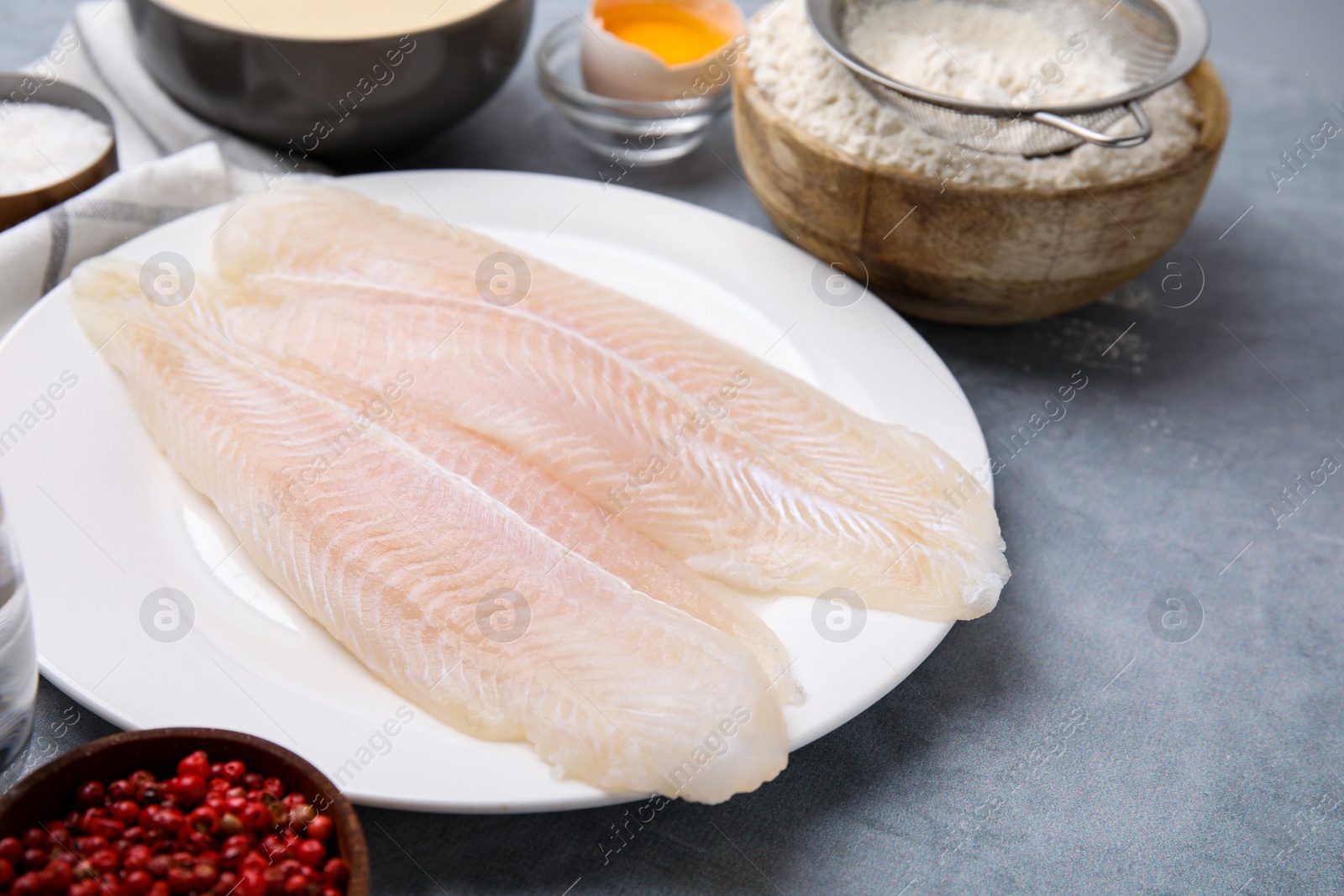 Photo of Different ingredients for batter and raw fish fillet on light grey table. Space for text