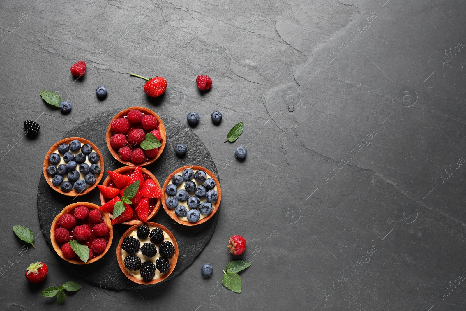 Photo of Tartlets with different fresh berries on black table, flat lay and space for text. Delicious dessert