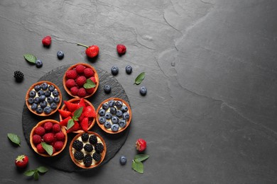 Tartlets with different fresh berries on black table, flat lay and space for text. Delicious dessert