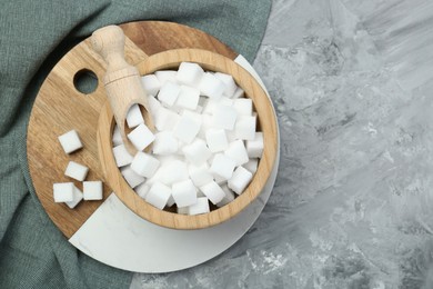 White sugar cubes in wooden bowl and scoop on grey table, top view. Space for text