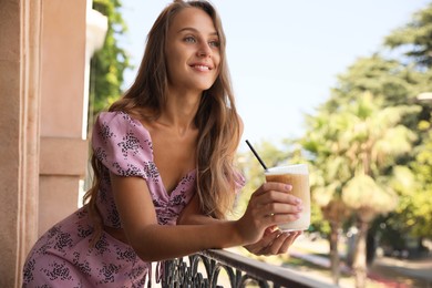 Photo of Beautiful young woman with glass of coffee standing on balcony, space for text