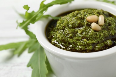 Photo of Bowl of tasty pesto and arugula on white table, closeup