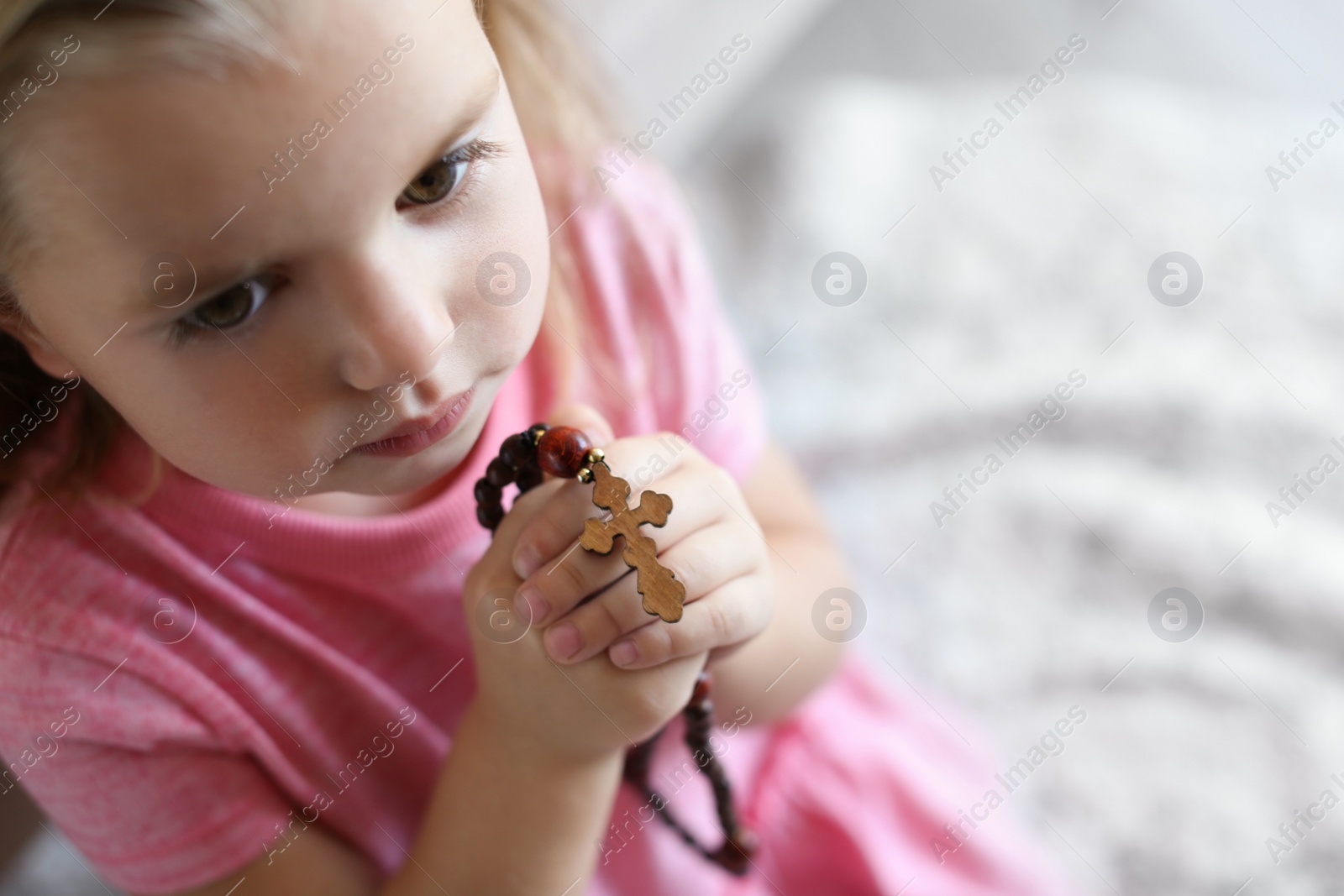 Photo of Cute little girl with beads praying on blurred background