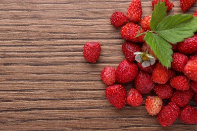 Photo of Pile of wild strawberries, flower and leaves on wooden table, flat lay. Space for text