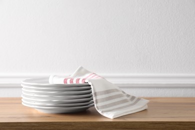 Photo of Kitchen towel and clean dishware on wooden table near white wall. Space for text