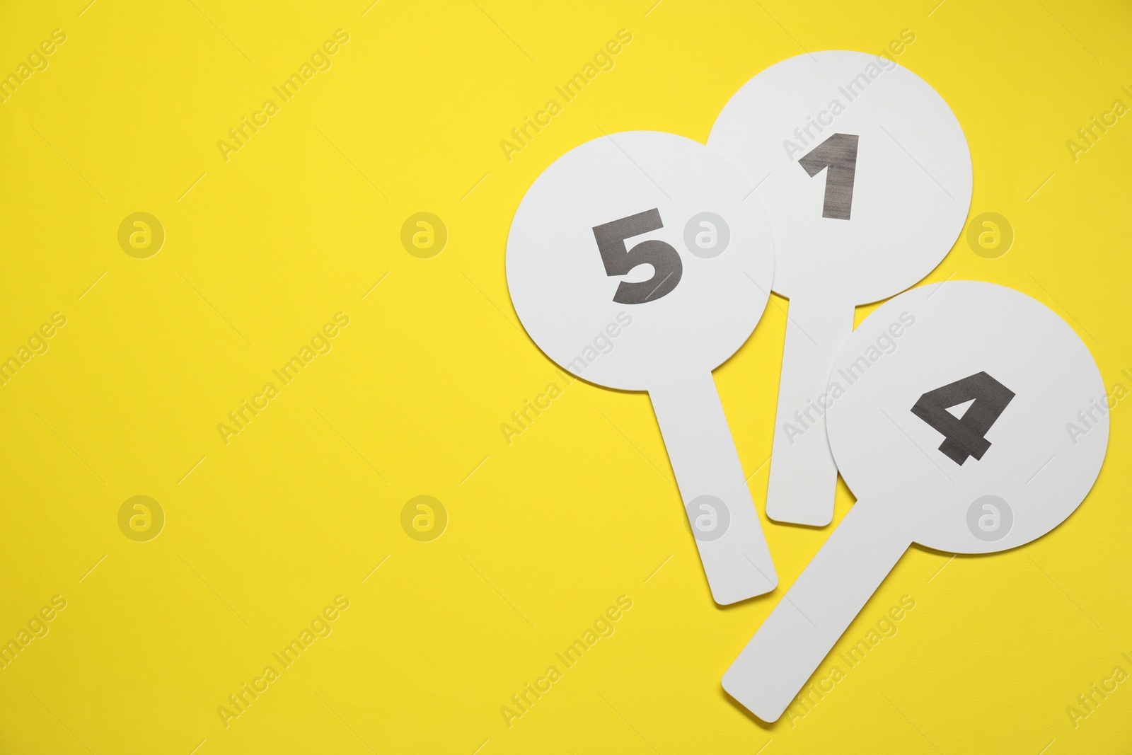 Photo of Auction paddles with numbers on yellow background, flat lay. Space for text