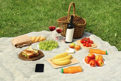 Photo of Wicker basket and food on blanket in park. Summer picnic