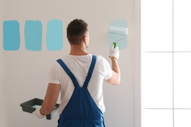 Man painting wall with light blue dye indoors, back view