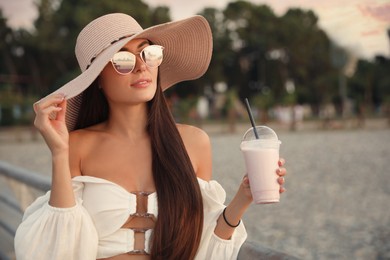 Beautiful young woman with tasty milk shake outdoors, space for text