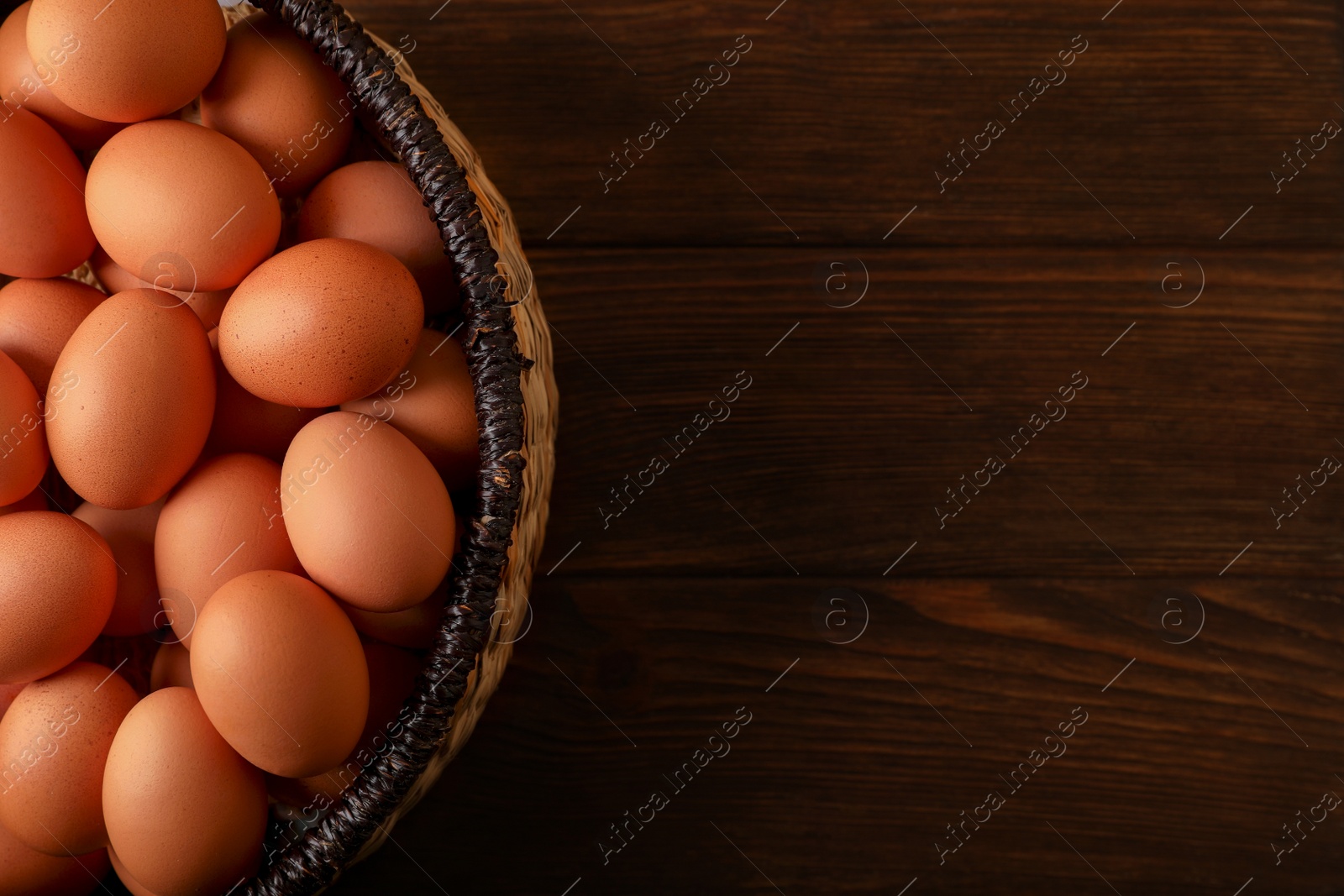 Photo of Raw chicken eggs in wicker basket on wooden table, top view. Space for text