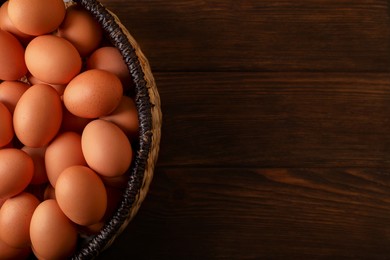 Raw chicken eggs in wicker basket on wooden table, top view. Space for text