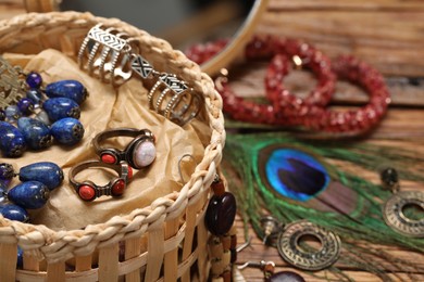 Photo of Jewelry box with many different accessories and peacock feather on wooden table, closeup