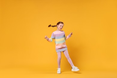 Cute little girl dancing on orange background