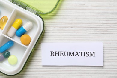 Photo of Card with word Rheumatism and pills on white wooden table, flat lay. Space for text