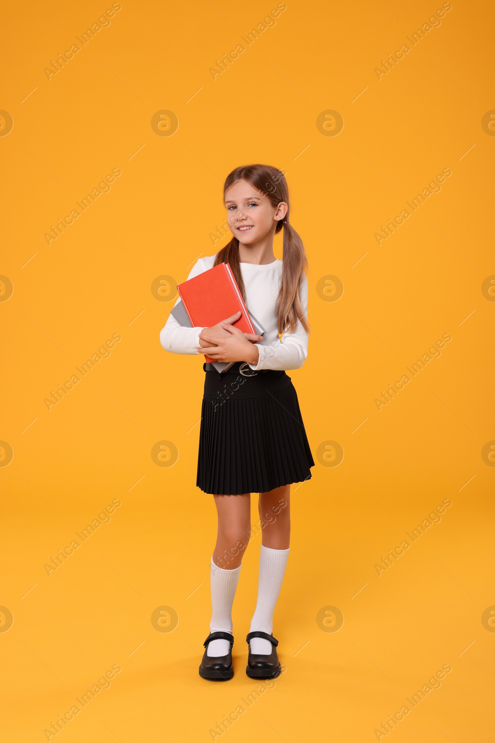 Photo of Happy schoolgirl with books on orange background