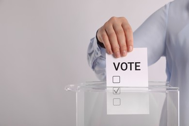 Woman putting paper with word Vote and tick into ballot box on light grey background