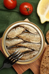 Photo of Canned sprats, tomatoes, lemon and fork on table, flat lay