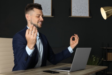 Photo of Businessman practicing zen yoga at table in office