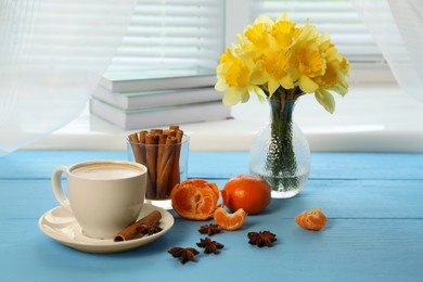 Beautiful yellow daffodils in vase, cup of coffee and tangerines on light blue wooden table