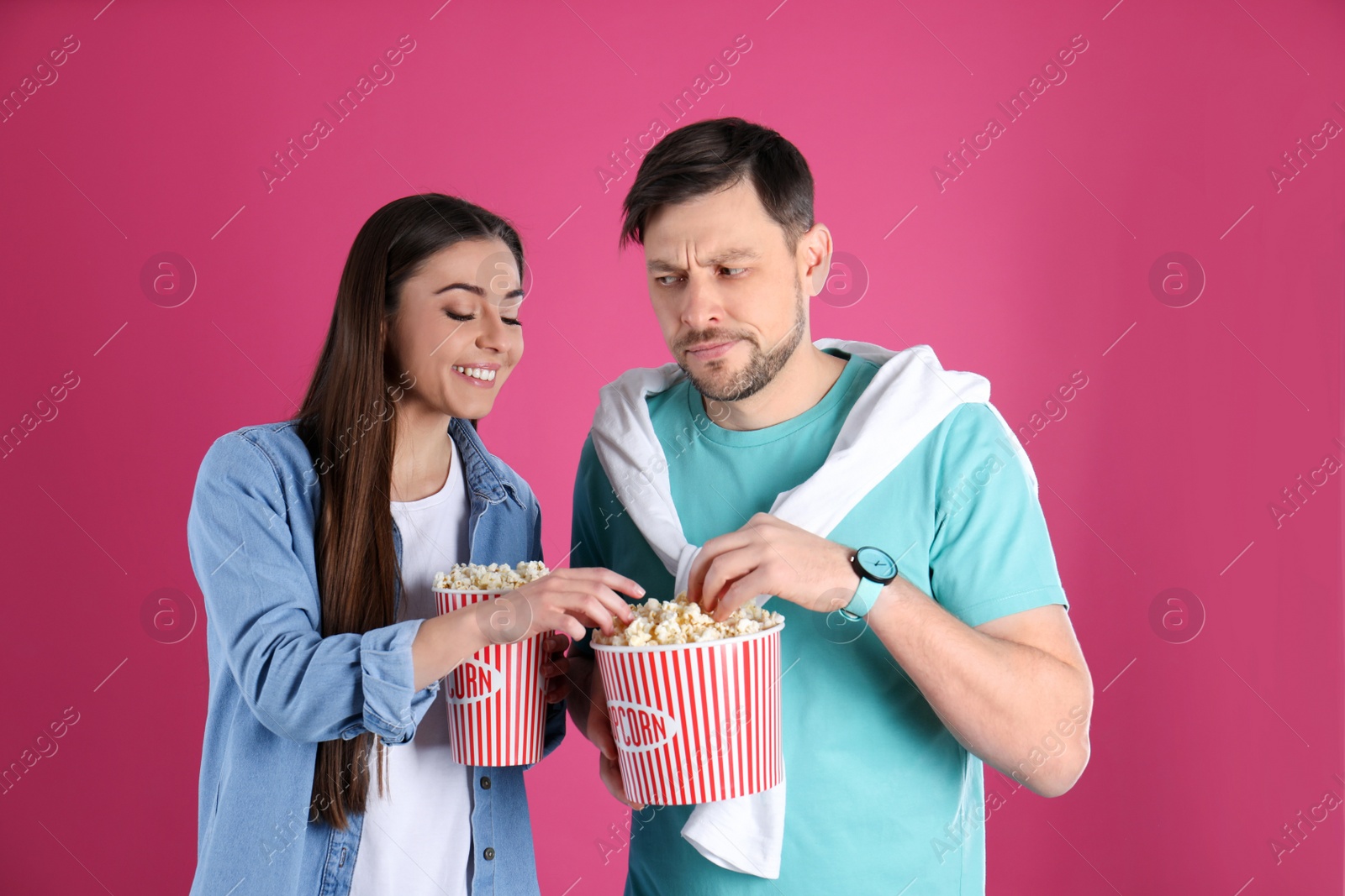 Photo of Young woman stealing popcorn from boyfriend on color background