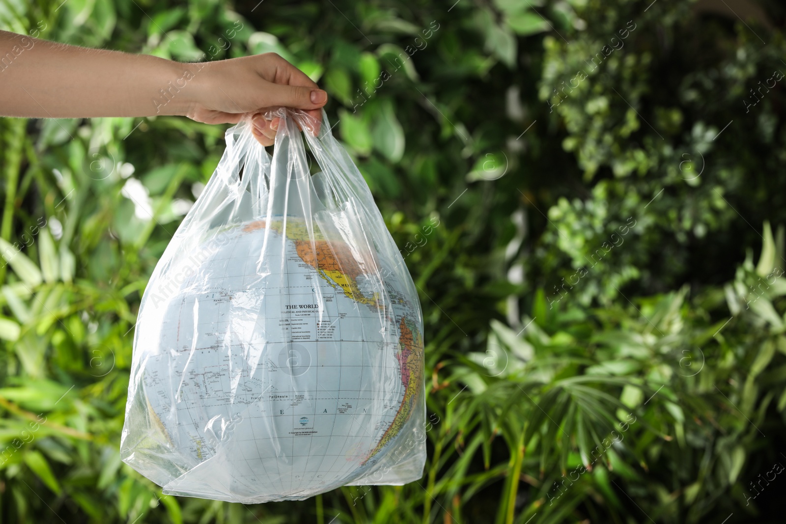 Photo of Woman holding globe in plastic bag against green leaves, closeup. Space for text. Environmental conservation