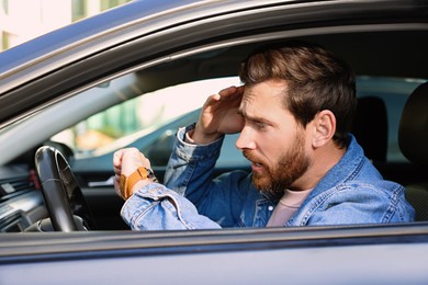 Photo of Emotional man checking time on watch in car. Being late concept