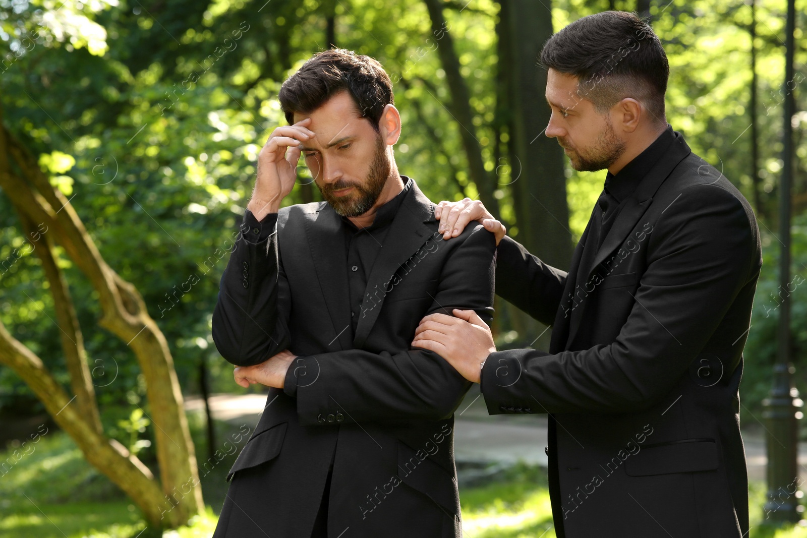 Photo of Funeral ceremony. Man comforting his friend outdoors
