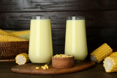 Photo of Tasty fresh corn milk in glasses and cobs on wooden table