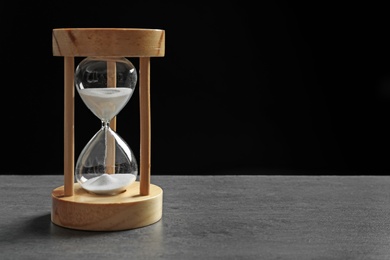 Hourglass with flowing sand on table against black background. Time management