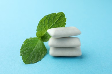 Tasty white chewing gums and mint leaves on light blue background, closeup