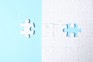 Photo of Blank white puzzle with separated piece on light blue background, flat lay