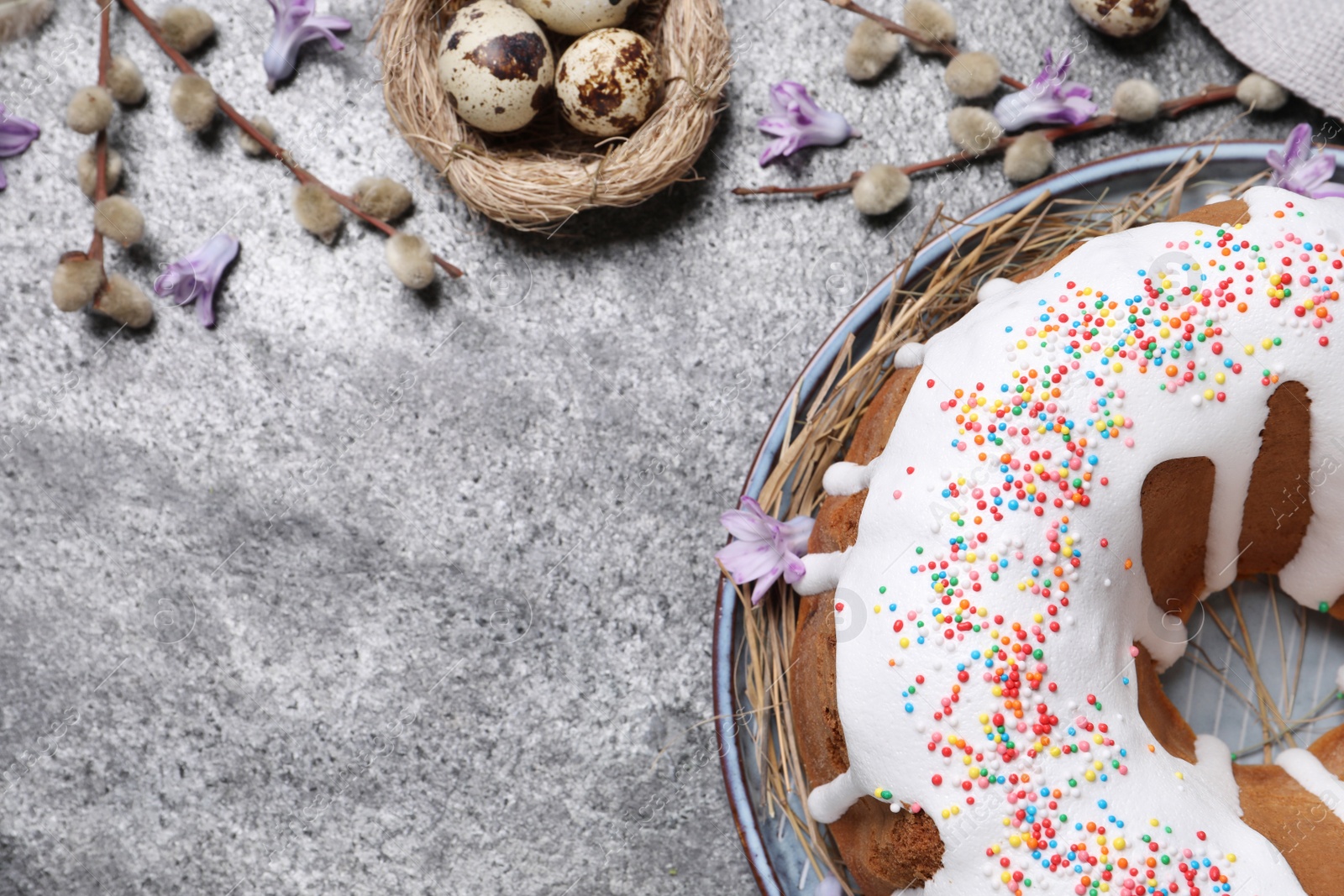 Photo of Glazed Easter cake with sprinkles and quail eggs on grey table, flat lay. Space for text