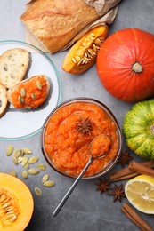 Delicious pumpkin jam and ingredients on grey table, flat lay