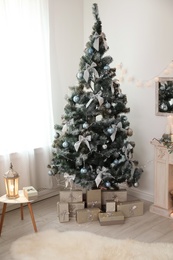 Decorated Christmas tree with gift boxes and lantern on table in stylish living room interior